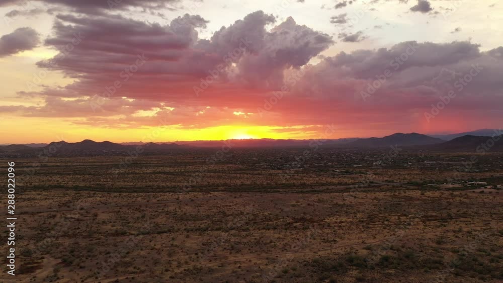 A drone descending over the open Sonoran Desert with a setting sun and rain clouds in the distance. A drone descending over the open Sonoran Desert with a setting sun and rain clouds in the distance.