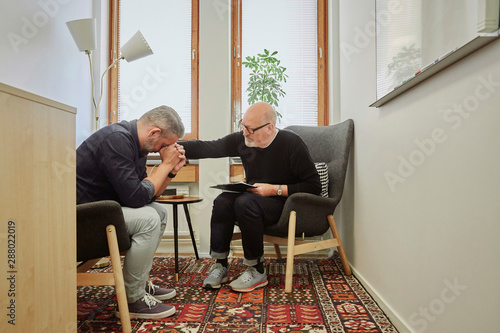 Therapist consoling mature patient during therapy session photo