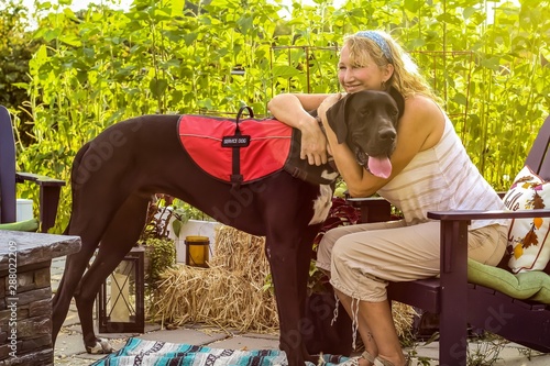 Older adult Caucasian woman with mobility issue is able to enjoy the outdoors on her patio with the help of her loyal and attentive Great Dane service dog by her side