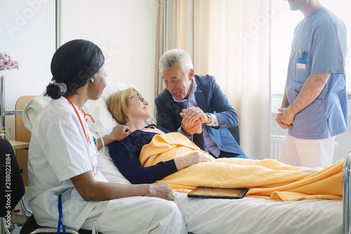Healthcare workers looking at senior man consoling patient in hospital ward