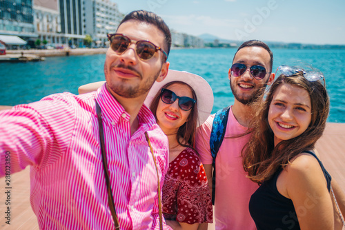 Couple of tourists is exploring new city together. Smiling and takeing a selfie, next to the sea. © qunica.com