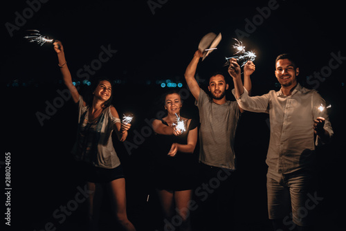 Happy friends lighting sparklers and enjoying freedom, low key, dark image