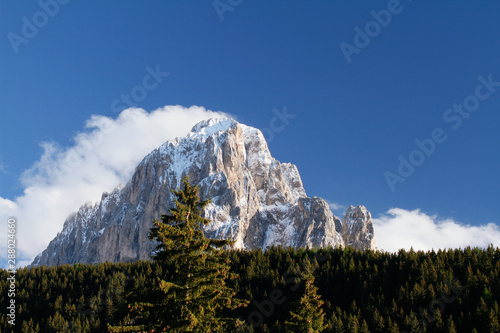 Langkofe, Sassolungo Snow covered peak with clouds hanging above the Mountain Peak. Thick Forest beneath the Sasso lungo, Lang kofel. Seen from Selva di Val Gardena photo