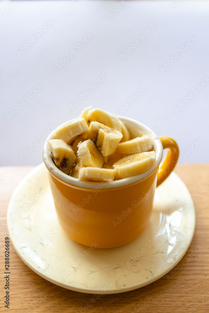 Healthy breakfast, yoghurt with slices of banana in a yellow mug on a beige plate