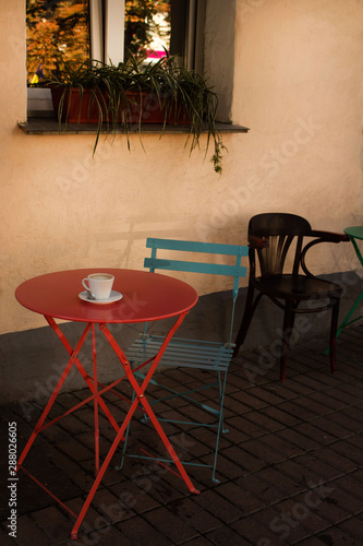 Street cafe - a round table with a cup of coffee on the background of a window with flowers on the windowsill