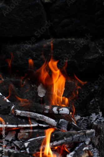 Burned Wood with flames still burning, dark Stone Background of camp fire or Grill. Raging flames