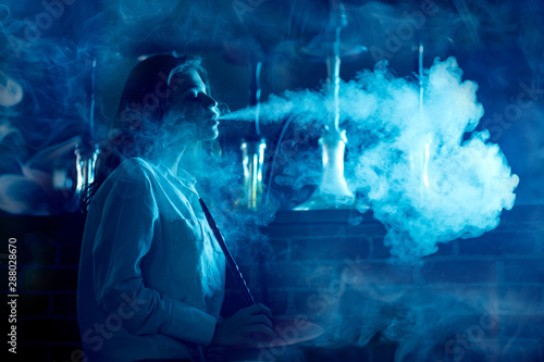 Beautiful woman in night club smoke hookah or shisha bar, blue background