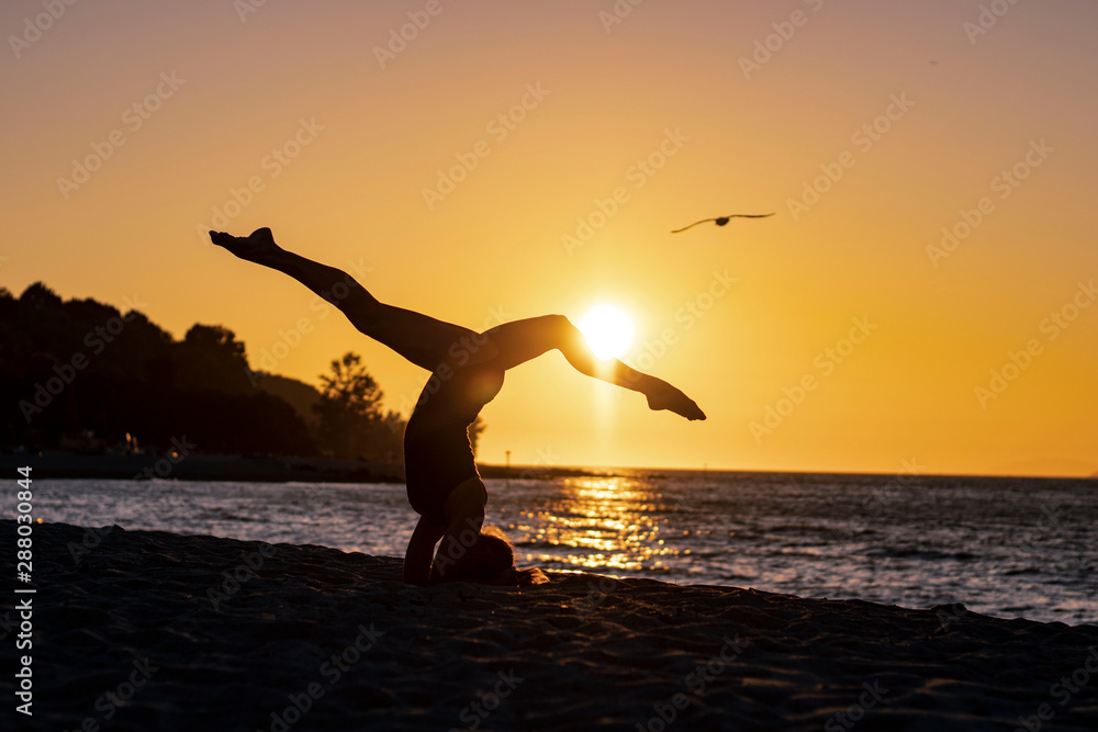 Woman doing yoga exercises asana on the sandy beach at sunset, zen, healthy and wellbeing, with a bird flying away