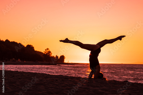 Woman practicing ashtanga yoga on the beach at sunset with pink sky in background, zen attitude, serenity, healthy an wellbeing