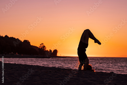 Flexible woman practicing yoga and gymnastics on the beach at sunset, posing scorpion, wellbeing, good posture, zen attitude, healthy, ocean pacific view