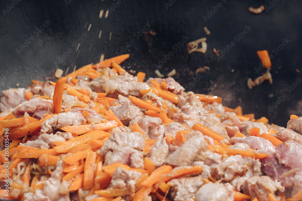 Process of cooking of delicious pilaf. View from above of tasty pieces of meat and healthy carrots roasting in cauldron during picnic in garden. Concept of cuisine and food. Process of cooking of delicious pilaf. View from above of tasty pieces of meat and healthy carrots roasting in cauldron during picnic in garden. Concept of cuisine and food.