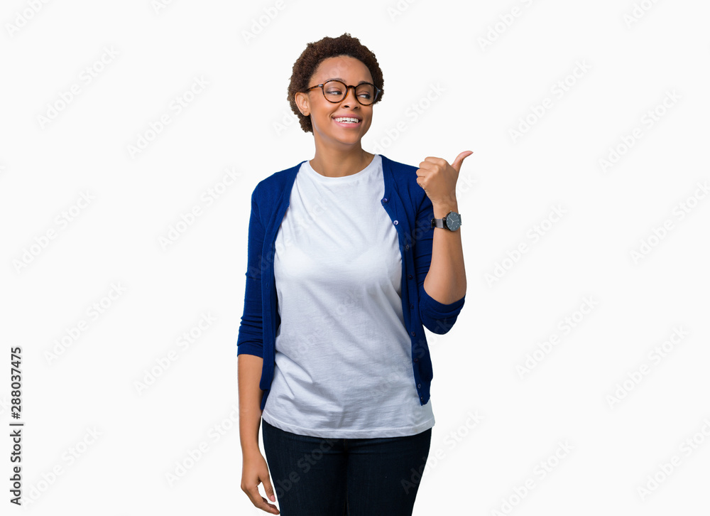 Young beautiful african american woman wearing glasses over isolated background smiling with happy face looking and pointing to the side with thumb up. Young beautiful african american woman wearing glasses over isolated background smiling with happy face looking and pointing to the side with thumb up.