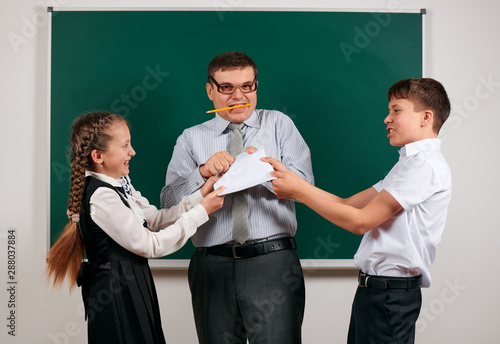 Portrait of a teacher checking homework, reading school exercise books, schoolboy and schoolgirl with old fashioned eyeglasses posing on blackboard background - back to school and education concept photo