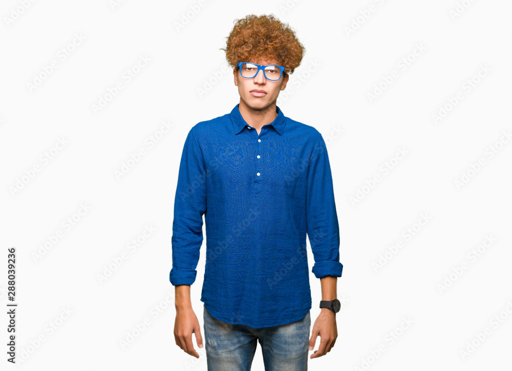 Young handsome man with afro hair wearing blue glasses with serious expression on face. Simple and natural looking at the camera. Young handsome man with afro hair wearing blue glasses with serious expression on face. Simple and natural looking at the camera.
