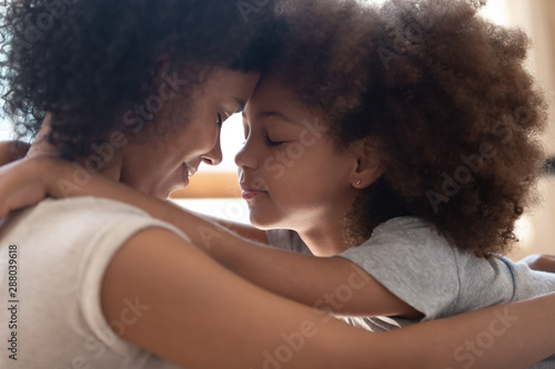 Mixed race mother touching foreheads with little cute daughter. photo