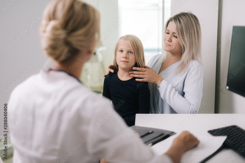 Mom with kid girl with blond hair at doctor in pediatrician appointment. Little girl with her mother at a doctor on consultation
