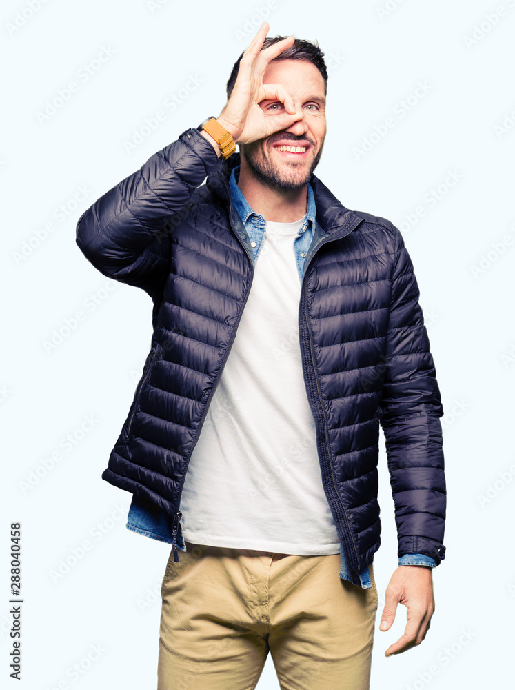Handsome man wearing winter coat doing ok gesture with hand smiling, eye looking through fingers with happy face. Handsome man wearing winter coat doing ok gesture with hand smiling, eye looking through fingers with happy face.