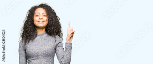 Young beautiful girl with curly hair showing and pointing up with finger number one while smiling confident and happy. © Krakenimages.com