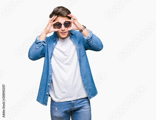 Young handsome man wearing sunglasses over isolated background Trying to open eyes with fingers, sleepy and tired for morning fatigue