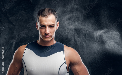 Portrait of muscular handsome man in wetsuit and with cloud of talc around over dark background.