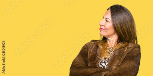 Beautiful middle age elegant woman wearing mink coat smiling looking to the side with arms crossed convinced and confident