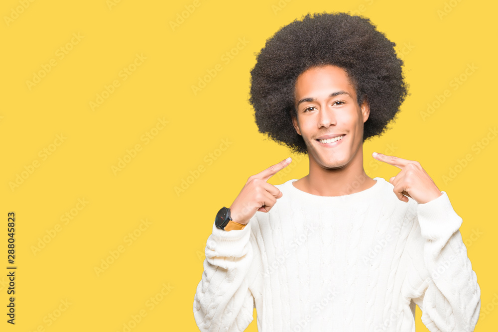 Young african american man with afro hair wearing winter sweater smiling confident showing and pointing with fingers teeth and mouth. Health concept. Young african american man with afro hair wearing winter sweater smiling confident showing and pointing with fingers teeth and mouth. Health concept.