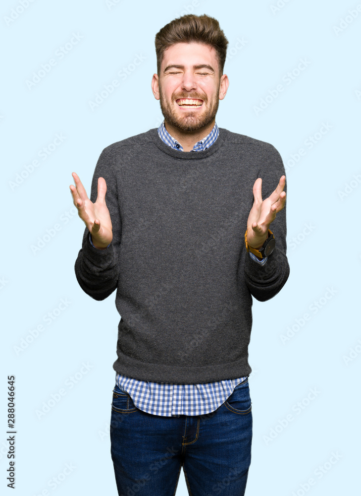 Fototapeta premium Young handsome elegant man celebrating mad and crazy for success with arms raised and closed eyes screaming excited. Winner concept