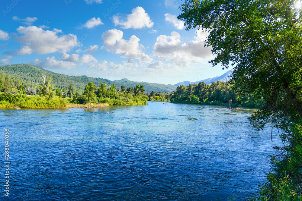 Two paddle boarders navigate the wide Wenatchee River near the town of Leavenworth, Washington in the Northwest of the United States of America.