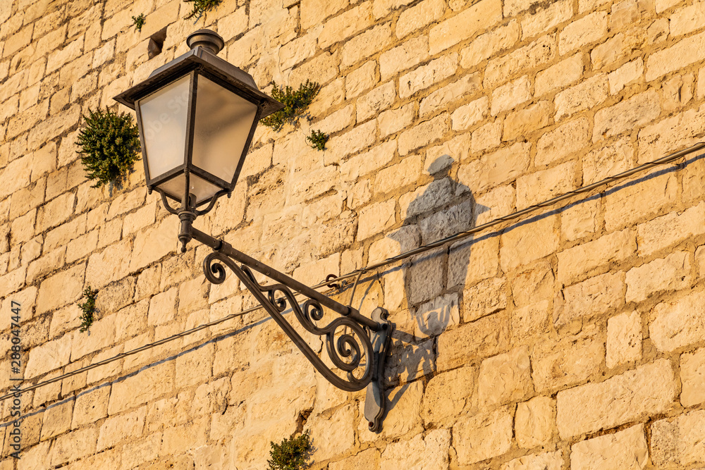 Italy, Apulia, Metropolitan City of Bari, Bari. Wrought-iron street lamp in a stone wall.