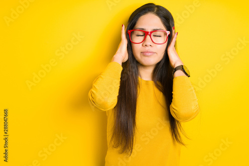 Beautiful brunette woman wearing red glasses over yellow isolated background suffering from headache desperate and stressed because pain and migraine. Hands on head.