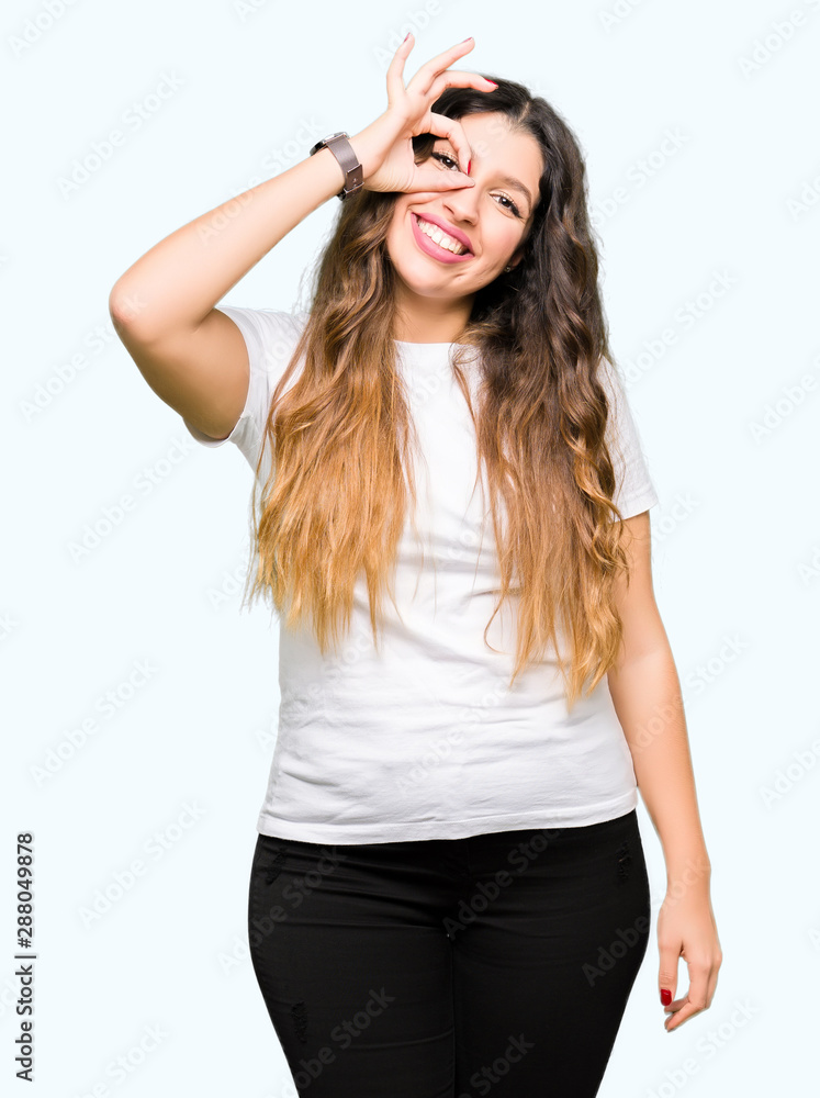 Young beautiful woman wearing casual white t-shirt doing ok gesture with hand smiling, eye looking through fingers with happy face. Young beautiful woman wearing casual white t-shirt doing ok gesture with hand smiling, eye looking through fingers with happy face.