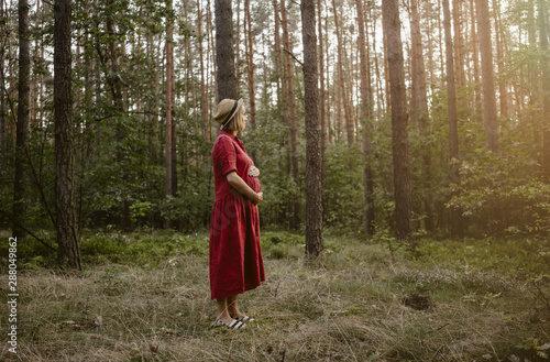 Blonde young pregnant woman in a red dress relaxing in a sunny forest