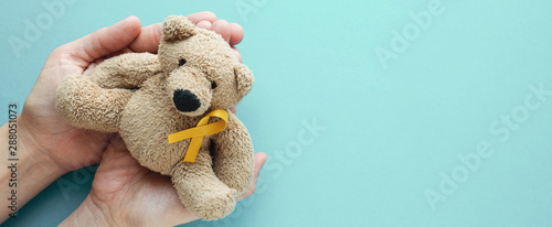 Hands holding children soft toy brown bear with yellow gold ribbon, Childhood cancer awareness