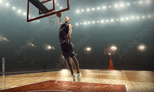 African american basketball player in action on a floodlit court. Slam dunk 