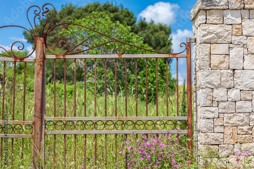 Italy, Apulia, Metropolitan City of Bari, Gioia del Colle. Rusty metal gate and stone wall.