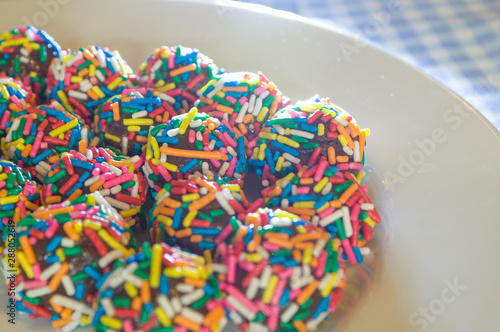 typical brazilian sweet at birthday parties, Brigadeiro, with colorful chocolate sprinkles on white plate