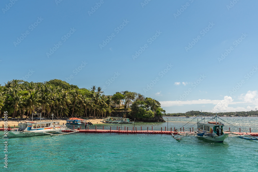 Manoc-Manoc, Boracay, Philippines - March 4, 2019: Cagban Jetty Port and floating pier with small outrigger tourist ferries vessels on azure sea, under blue sky with green horizon foliage.