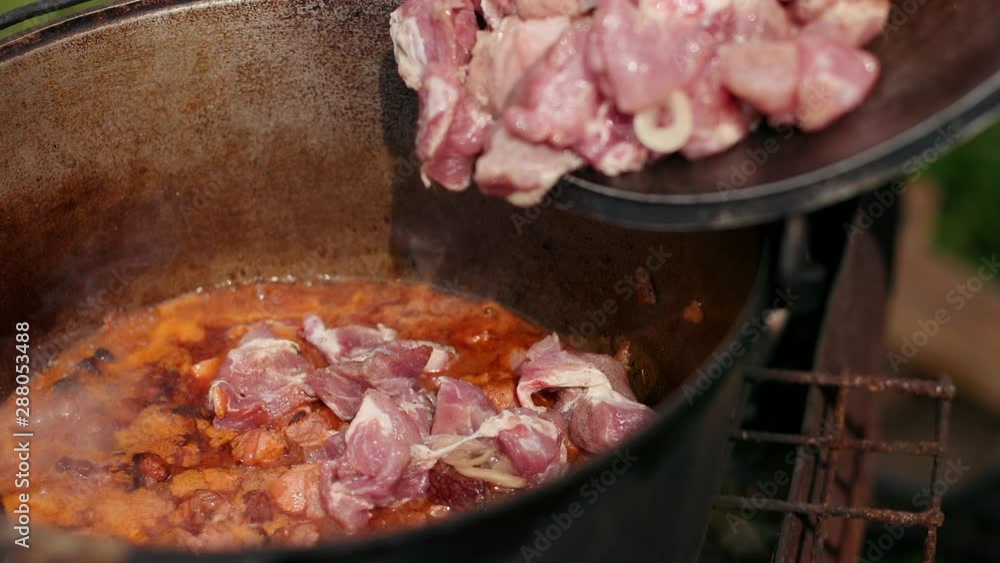 in large cast iron pot preparing dish, red with meat onions and other components in large cast iron pot preparing dish, red with meat onions and other components