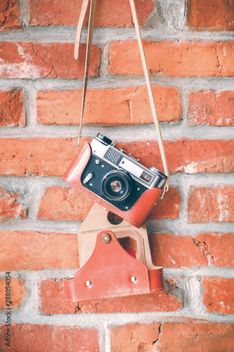Vintage analog film camera with lens on a brick wall background.