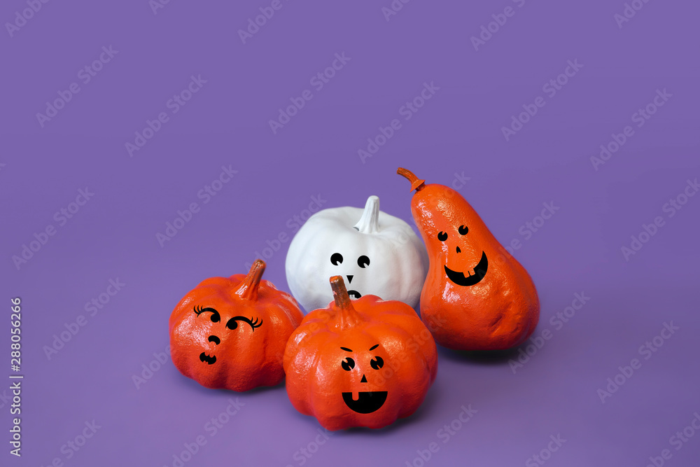 Obraz premium Pumpkins with funny faces on violet background, creative concept. Festive advertising flat lay banner, front view. Decor for celebration. Modern trendy halloween composition with copy space