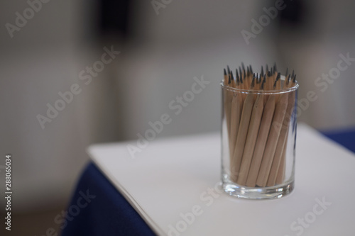 Glass Cup with brown and black pencils on the glass table. Close up.