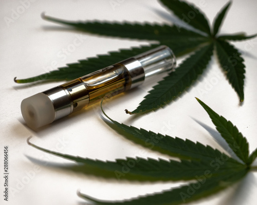 A CBD oil vape cartridge with hemp leaves on white background.