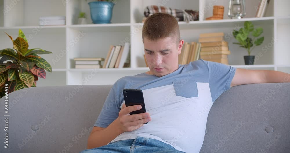 Closeup portrait of adult attractive caucasian man browsing on phone sitting on couch indoors Closeup portrait of adult attractive caucasian man browsing on phone sitting on couch indoors