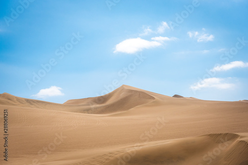 The swirling sand dunes of the Peruvian desert with light fluffy clouds above on a warm sunny day creating a spectacular contrast across the horizon