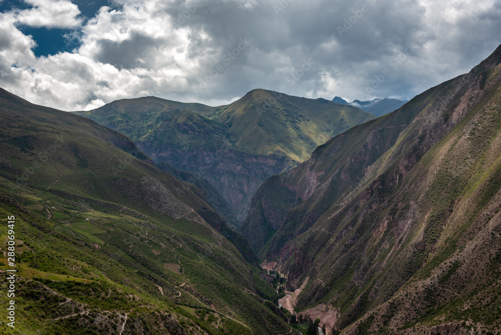 Deep within the Sacred Valley of Ollantaytambo, where the river flows between the mountains bringing life to the surrounding forests on a partially cloudy day Deep within the Sacred Valley of Ollantaytambo, where the river flows between the mountains bringing life to the surrounding forests on a partially cloudy day