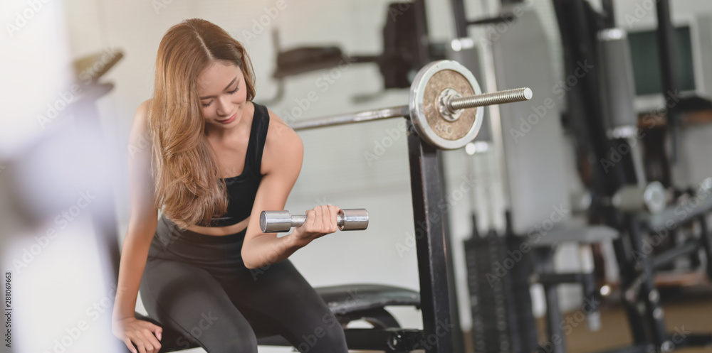 Obraz premium Beautiful asian athletic woman lifting weights at the gym and smiling at the camera