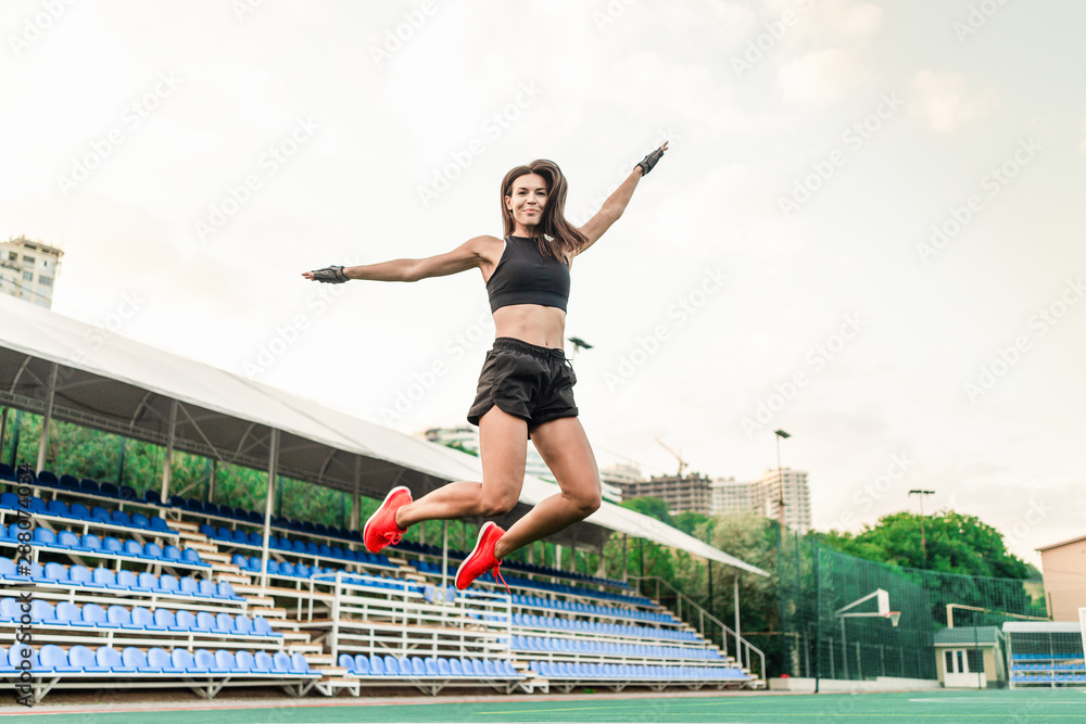 beautiful fit sporty woman jumping on the stadium high in the air
