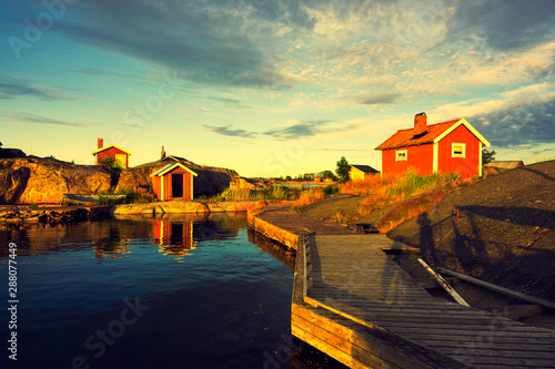 Traditional red wooden house in the island with bridge at sunset clouds sky in Sweden