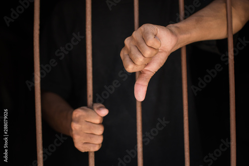 hand man thumbs down and hold steel in jail on black background.concept for prisoner,sadness,detain,erroneousness