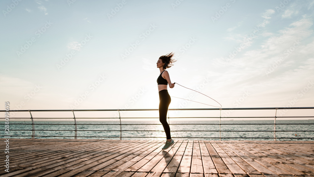 fit teenage girl with jump rope on a beach exercising and working out - obrazy, fototapety, plakaty 